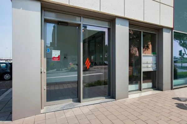 Voordeur van het ALEASE-kantoor aan de Laan der Verenigde Naties met reflectie van geparkeerde auto's in het glas.